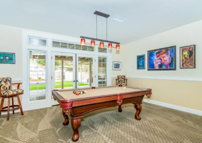 A pool table room with drop down lighting, 2 bar chairs, and artworks on the walls, tyler media works, real estate photography