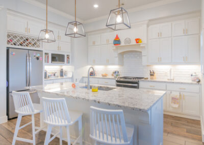 A kitchen with granite countertops, white cabinets, white high back bar chairs, wood floors and a stainless steel fridge, tyler media works, real estate photography