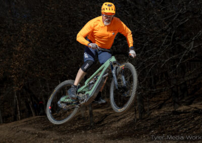guy on a mountain bike with orange shirt and orange helmet going over a jump