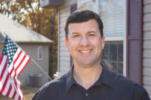 headshot of man with amercian flag in the background